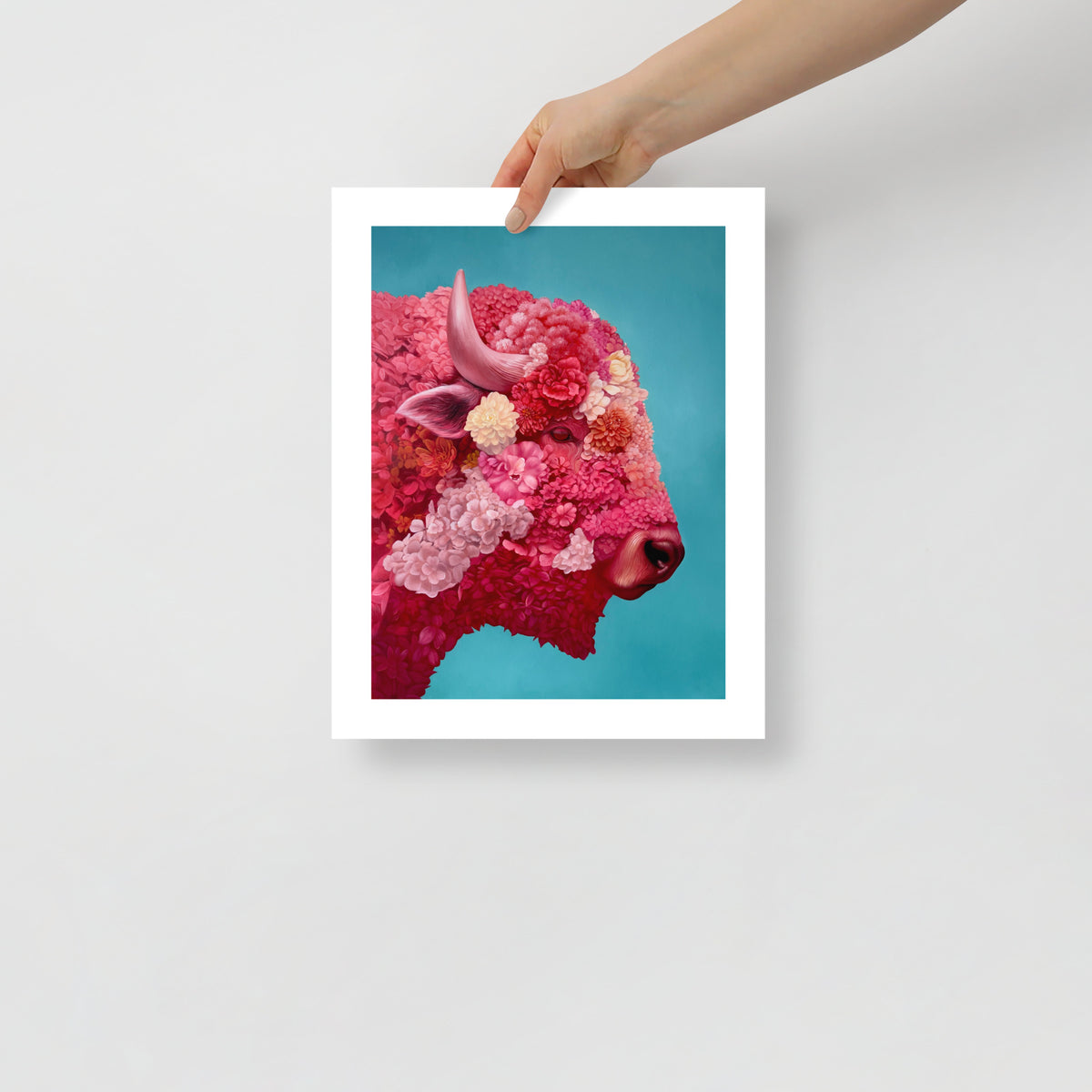 MEFREEK Seth Jennemann Open Edition Print Armor For A Hopeless Charge unframed art print held by hand showing a detailed floral bison portrait in vivid pink and red tones against a clean turquoise background, modern hyperreal surreal oil painting.