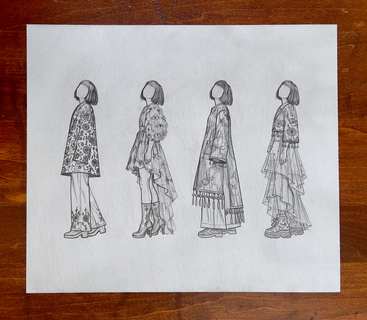 MEFREEK Seth Jennemann Original Pencil Drawing A Fire Escape Made Of Punchlines AKA A Life Jacket Full Of Laughter – Graphite pencil fashion croquis featuring four full-length, faceless female figures arranged side by side, each with a short bob haircut and a distinct outfit. The first wears a floral-patterned coat over wide-leg trousers with decorative embroidery. The second features a layered asymmetrical dress with illustrated eye motifs on its puffed sleeves, paired with tall heeled boots. The third wea