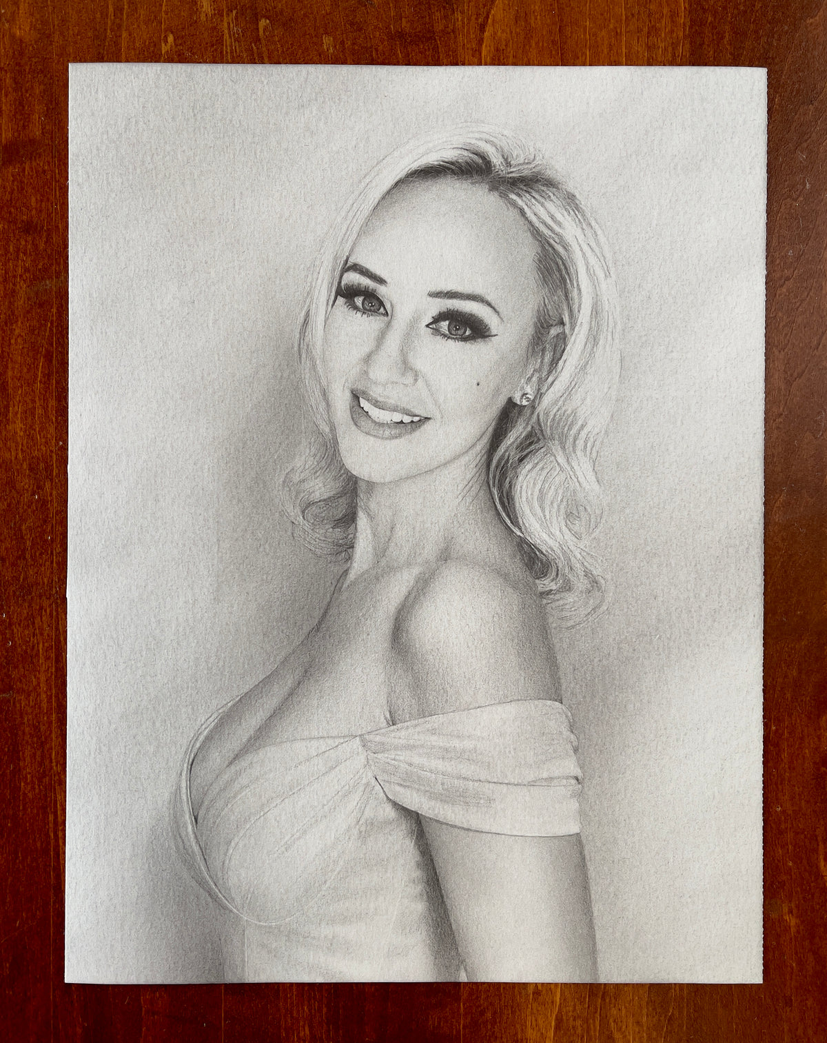 MEFREEK Seth Jennemann Original Pencil Drawing A Poorly Researched Autobiography – Realistic graphite pencil portrait of a smiling woman with shoulder-length, softly curled blonde hair, expressive eyes, long dark eyelashes, arched eyebrows, and a small beauty mark on her cheek. She poses in a three-quarter view, turning her face toward the viewer while wearing an elegant off-the-shoulder dress with gathered fabric across the bust. Fine pencil strokes, smooth tonal gradients, and delicate shading create life