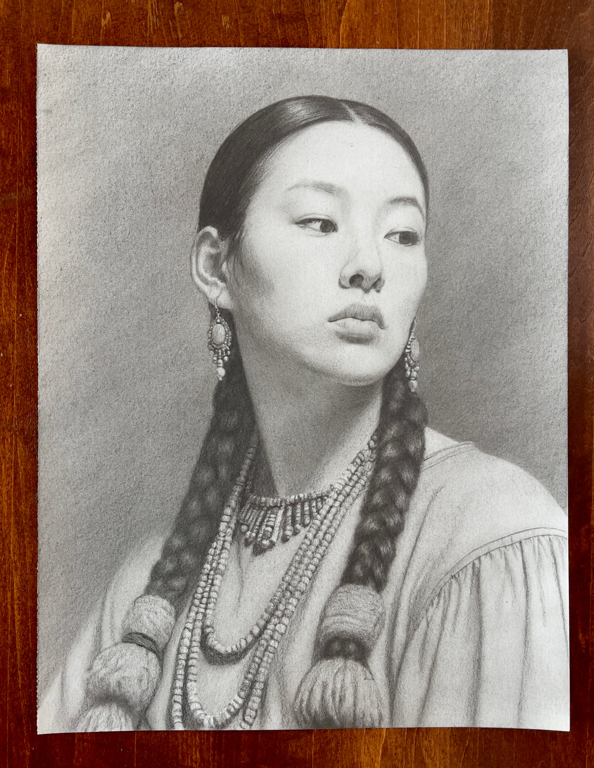 MEFREEK Seth Jennemann Original Pencil Drawing Afterlife Of Small Talk – Realistic graphite pencil portrait of a young Asian woman with sleek, center-parted dark hair styled into two thick braids ending in large wrapped tassels. Her head is turned slightly to the side as she gazes off to the right with a composed, contemplative expression. She wears ornate dangling earrings, multiple strands of beaded necklaces, and an intricately detailed beaded collar over a softly draped garment with gathered sleeves. De