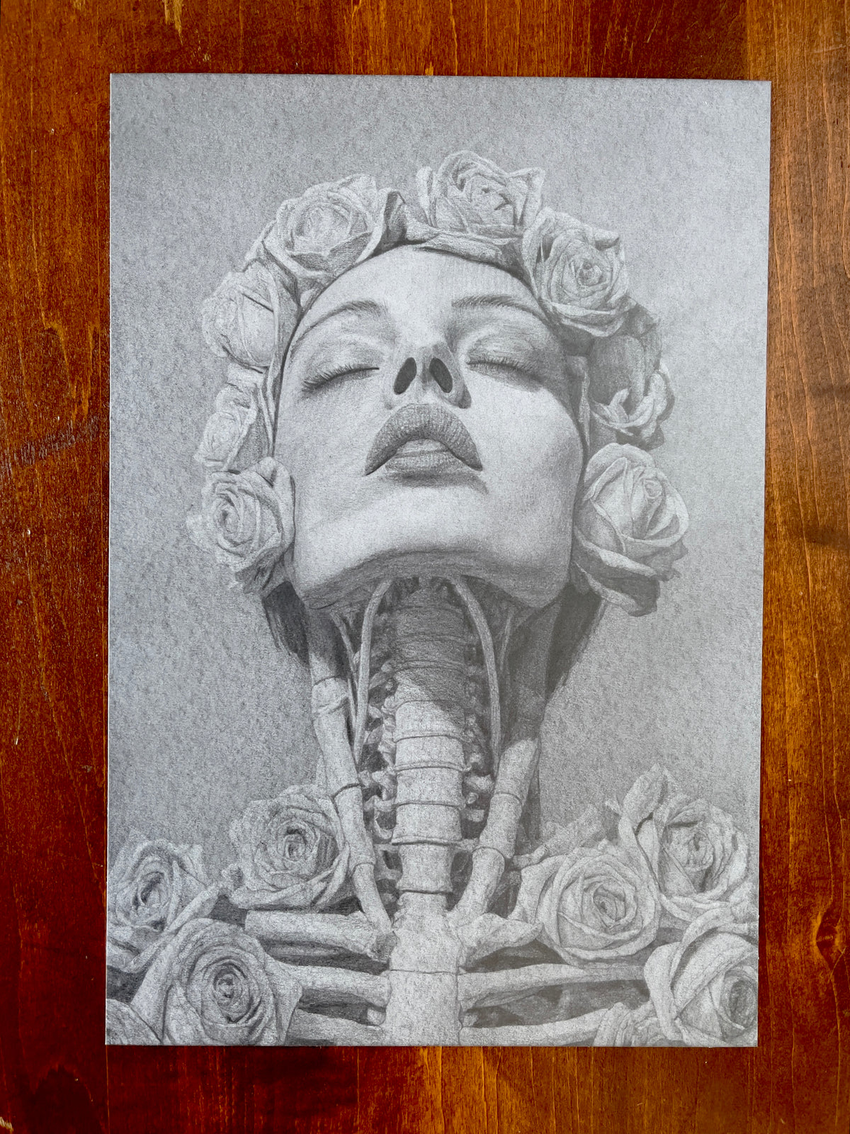 Seth Jennemann MEFREEK – “All That’s Left Is To Let Go” – graphite drawing in hyperreal pop surrealism style. A woman’s head adorned with roses tilts upward in calm surrender, her exposed throat and ribcage blending anatomy with floral forms, rendered in soft grayscale tones.
