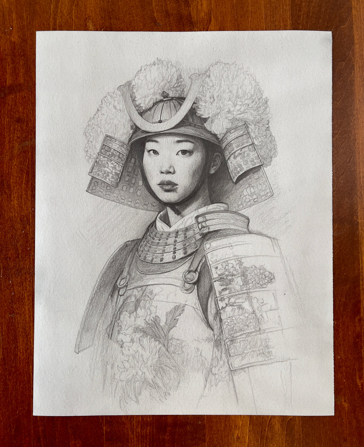 MEFREEK Seth Jennemann Original Pencil Drawing Best Wishes From A Safe Distance – Detailed graphite pencil portrait of a young Asian woman wearing ornate Japanese samurai-inspired armor adorned with floral designs and oversized chrysanthemum blossoms. Her elaborate kabuto helmet features a prominent gold-inspired crescent crest, large chrysanthemum arrangements, and decorative layered side guards with intricate patterns. She faces forward with a calm, composed expression, softly shaded facial features, almo