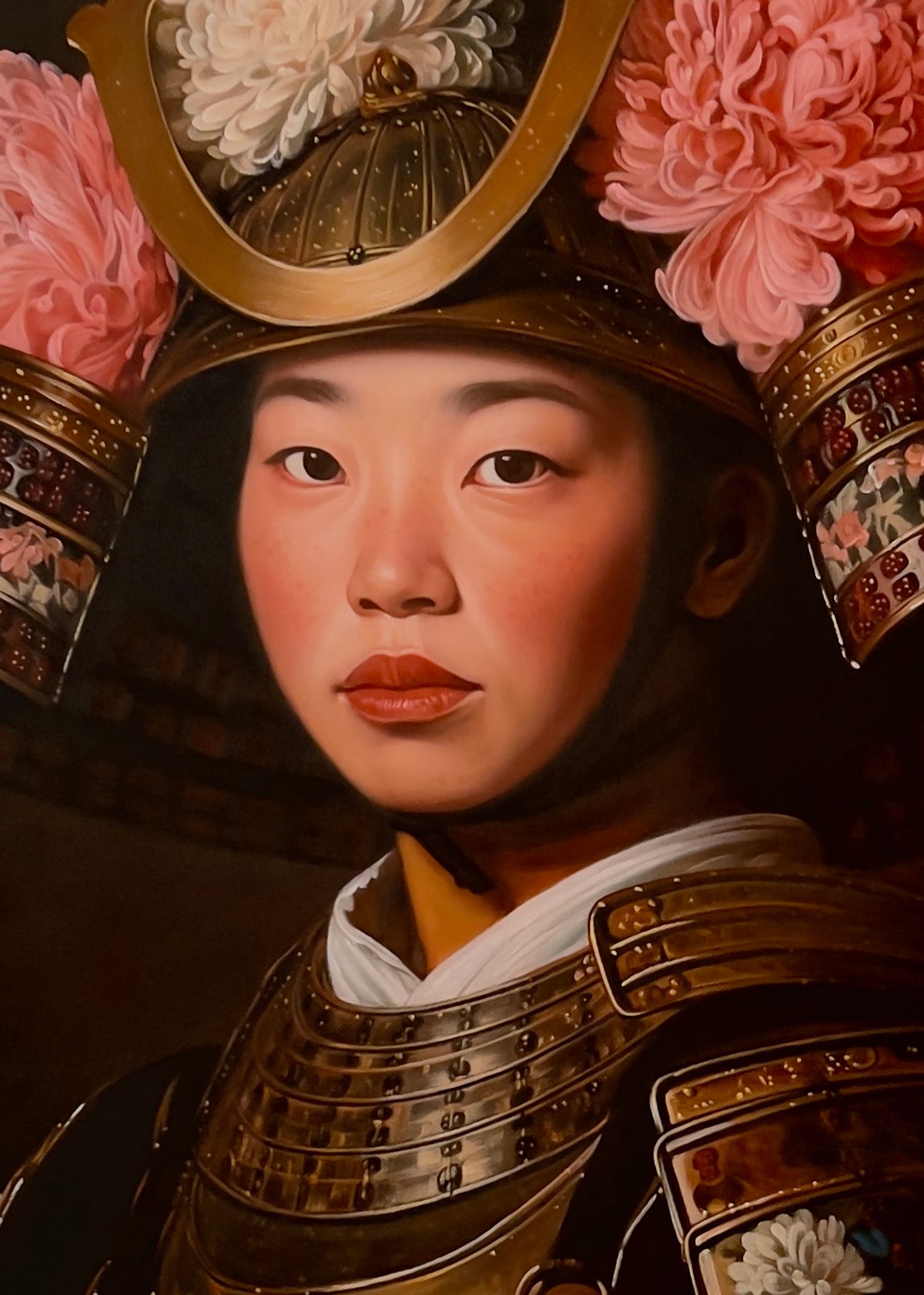 MEFREEK Seth Jennemann Original Oil Painting Best Wishes From A Safe Distance – Close-up portrait of a young Asian woman wearing ornate bronze and gold Japanese samurai armor and an elaborate helmet crowned with large pink and white chrysanthemums. Her softly illuminated face, dark brown eyes, rosy cheeks, and muted red lips contrast with the intricate metallic plates, floral decorations, and deep black background. The detailed oil painting combines realistic portraiture with delicate flowers and traditiona