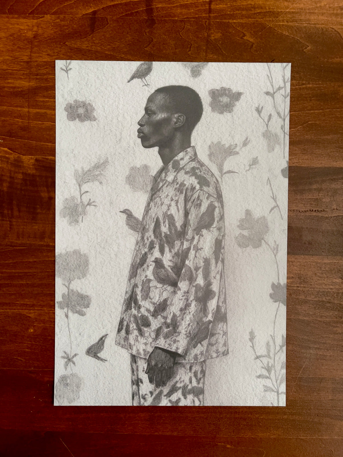 Seth Jennemann MEFREEK Every Door Looks Like A Trap – graphite drawing in hyperreal contemporary portrait style depicting a man in profile wearing a suit adorned with bird motifs, surrounded by softly rendered floral and avian forms that merge nature with elegance.
