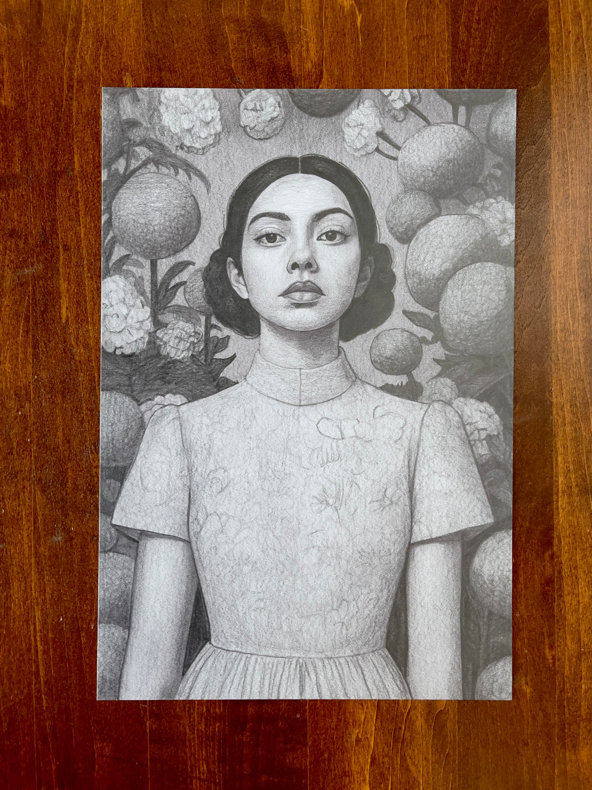 Seth Jennemann MEFREEK How To Leave Without Leaving – graphite drawing in hyperreal pop surrealism style portraying a poised woman in a floral-textured dress surrounded by oversized spherical fruit and blossoms, blending botanical surrealism with serene portraiture.
