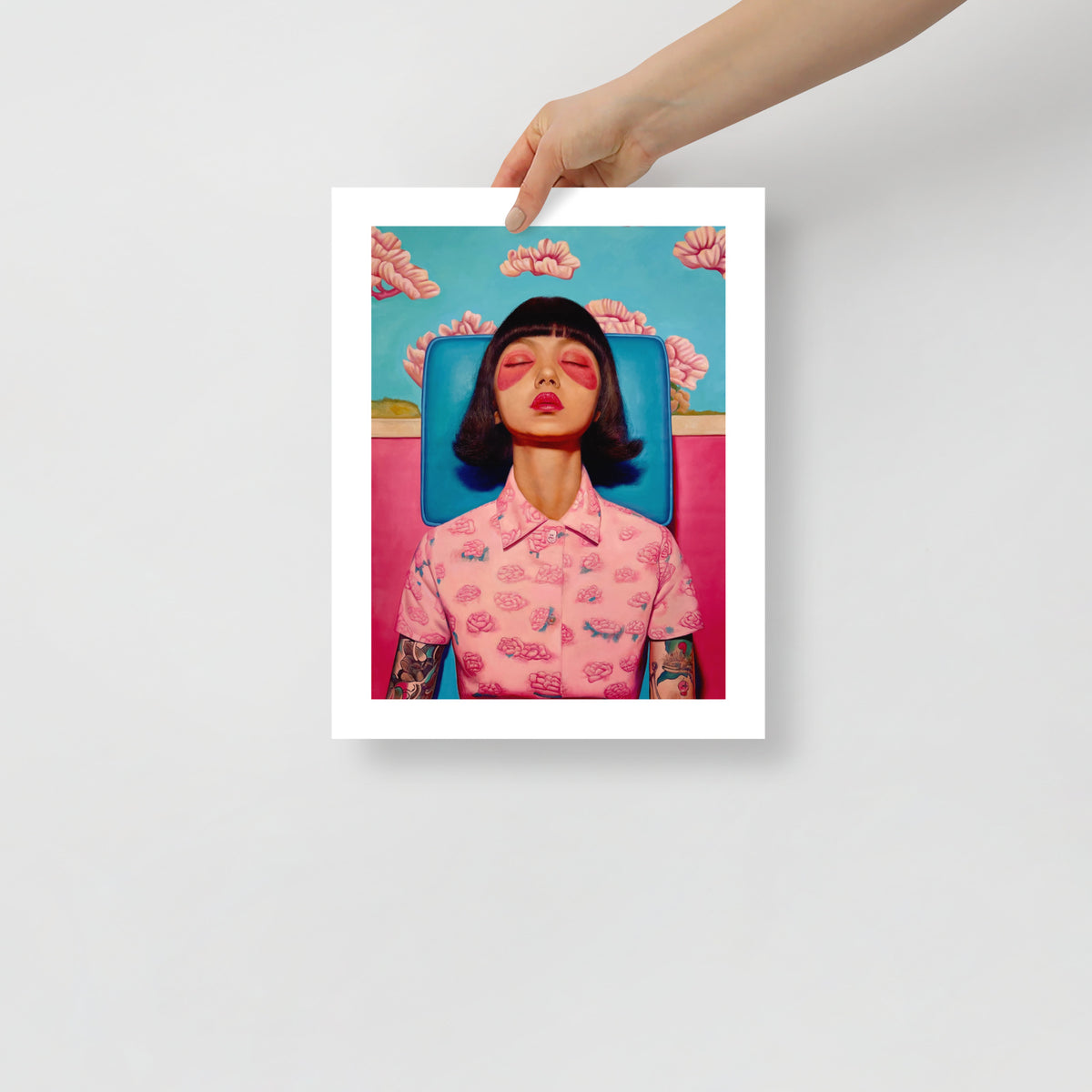 MEFREEK Seth Jennemann Open Edition Print “Infinity Loops And Other Dead Ends” — contemporary fine art print featuring a woman in a pink floral shirt with tattoos, sitting in a blue chair against a bright pink wall, shown unframed and held by a person.