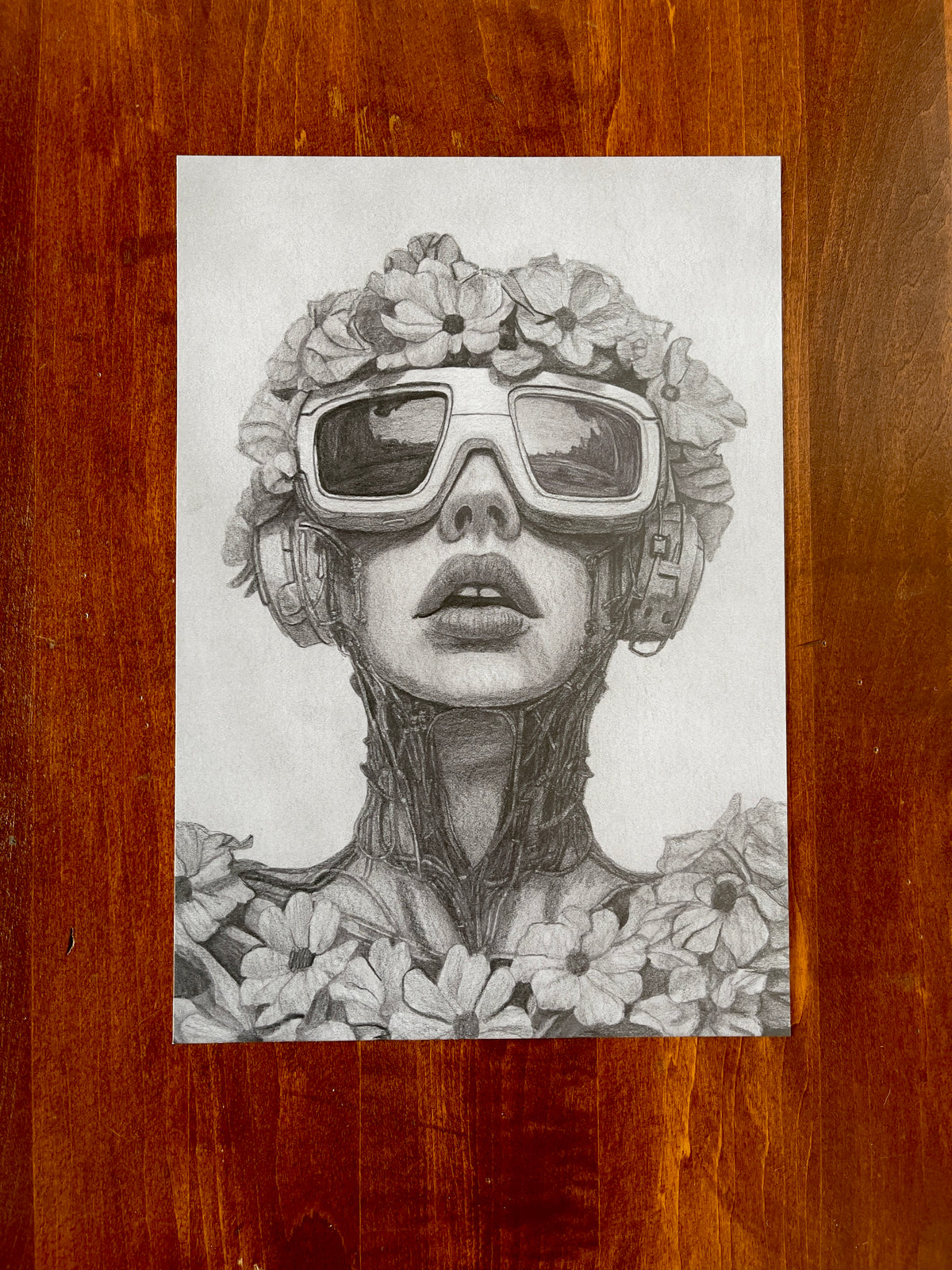 Seth Jennemann MEFREEK I Kill, Therefore I Am – graphite drawing in a hyperreal pop surrealism style portraying a cyborg woman with reflective goggles, floral headpiece, and mechanical neck, merging organic petals with intricate robotic detail.
