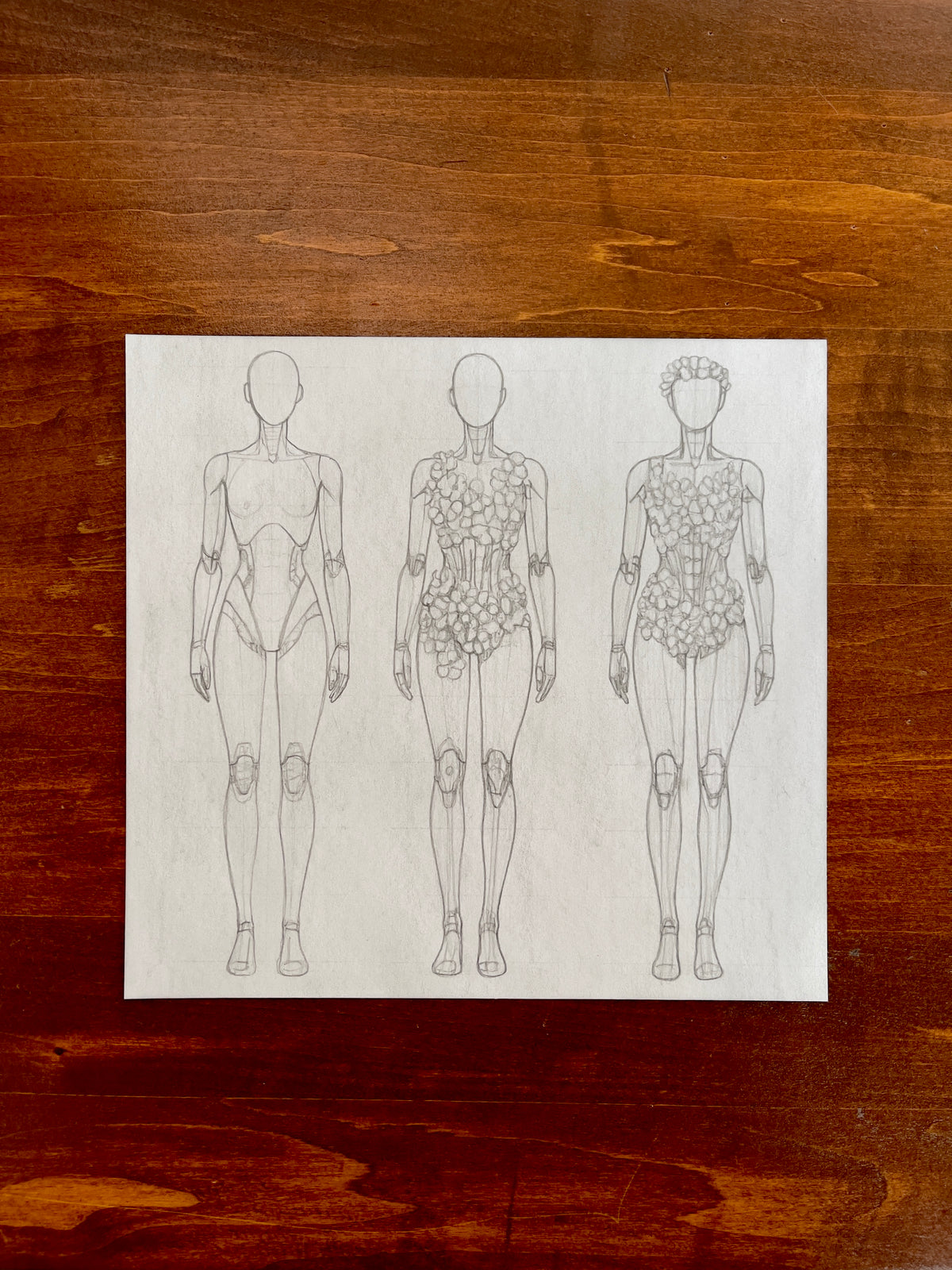 Seth Jennemann MEFREEK — Identity Program, graphite pencil fashion illustration in conceptual sketch style. Three robotic figures display avant-garde body designs evolving from mechanical frameworks to floral-integrated forms, symbolizing the fusion of technology and nature through detailed linework.