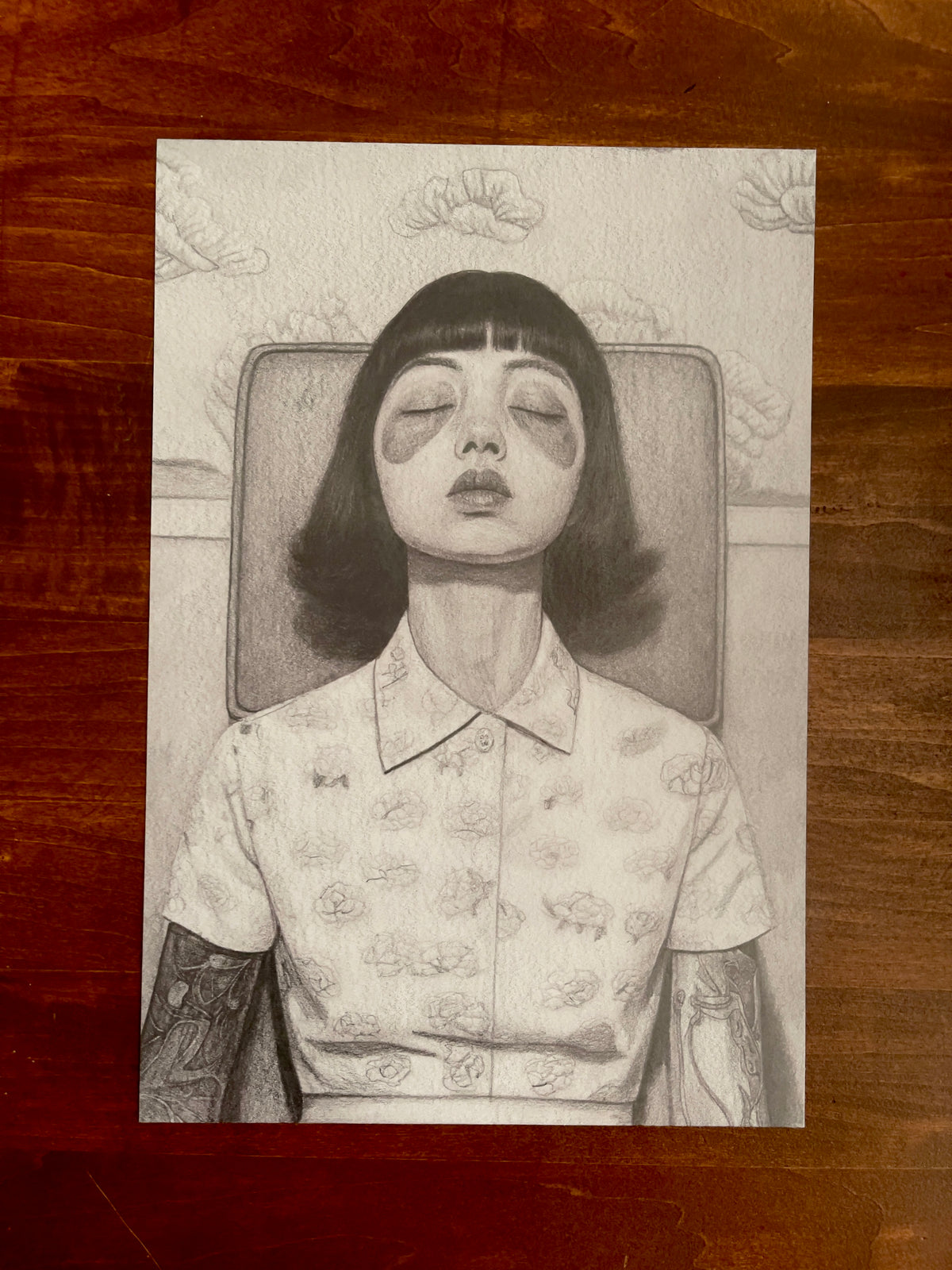 Seth Jennemann MEFREEK Infinity Loops And Other Dead Ends – graphite drawing in hyperreal pop surrealism style depicting a young woman with dark bobbed hair and closed eyes, wearing a floral-patterned collared shirt and sitting against a chair, evoking dreamlike stillness and quiet introspection.
