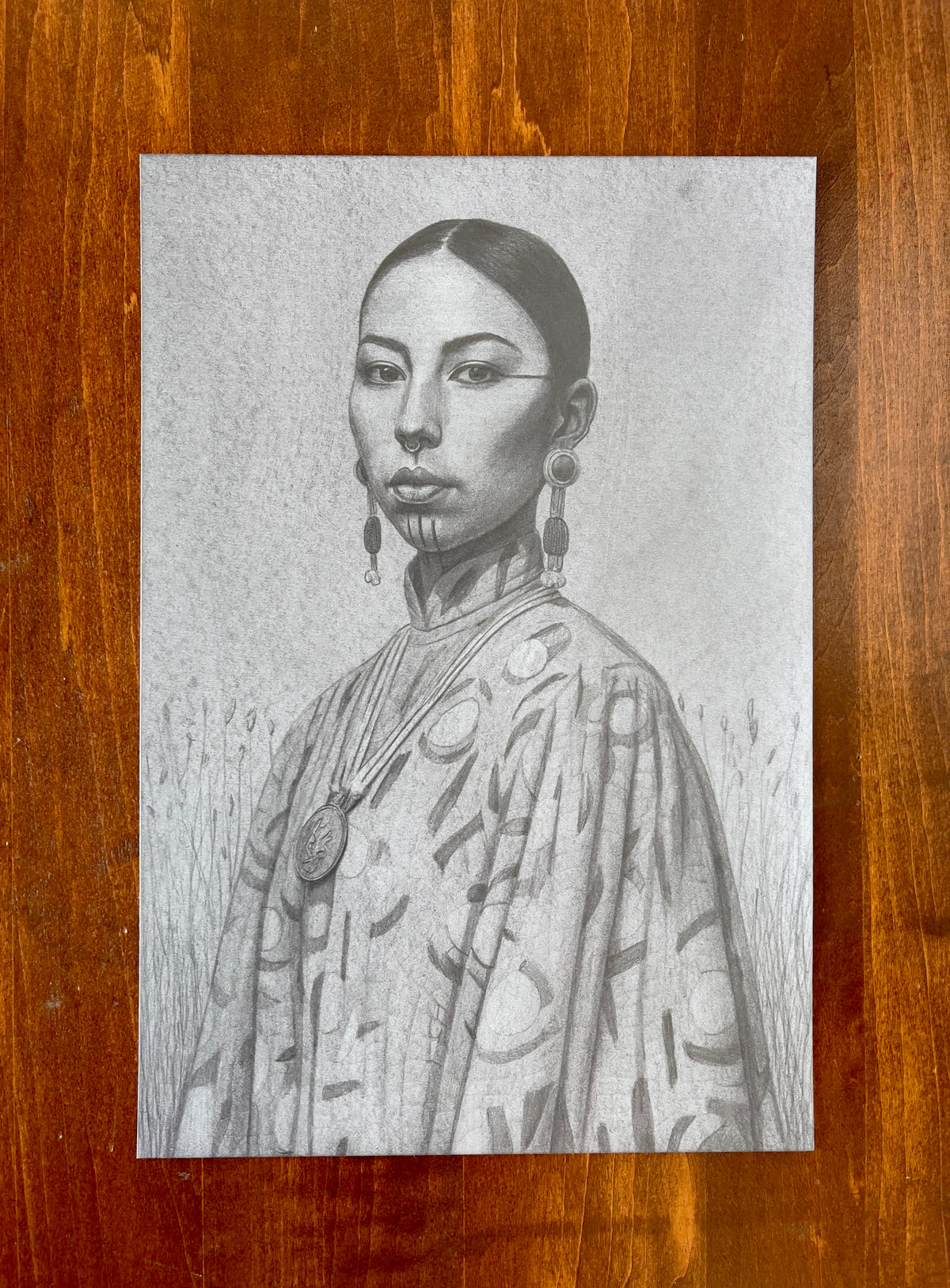 Seth Jennemann MEFREEK Quannah Chasinghorse – graphite drawing in hyperreal contemporary portrait style depicting an Indigenous woman with facial markings, bold earrings, and patterned ceremonial attire, combining realism and cultural symbolism in detailed pencil rendering.
