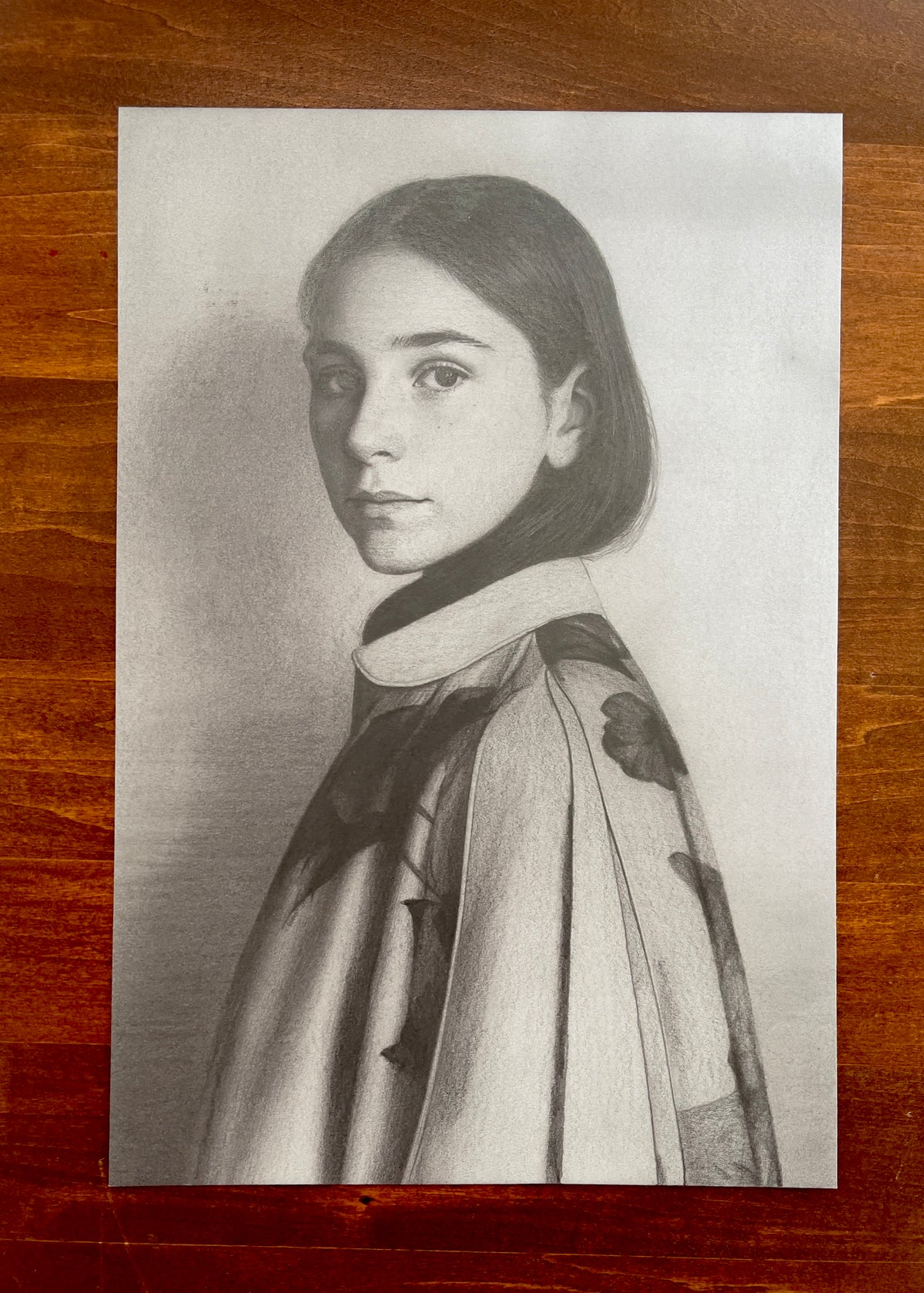 Seth Jennemann MEFREEK Rome Wasn't Programmed In A Day – graphite drawing in hyperreal contemporary portrait style depicting a young woman in three-quarter view wearing a sculptural coat with floral patterns, detailed rendering and soft tonal depth emphasizing realism and texture.
