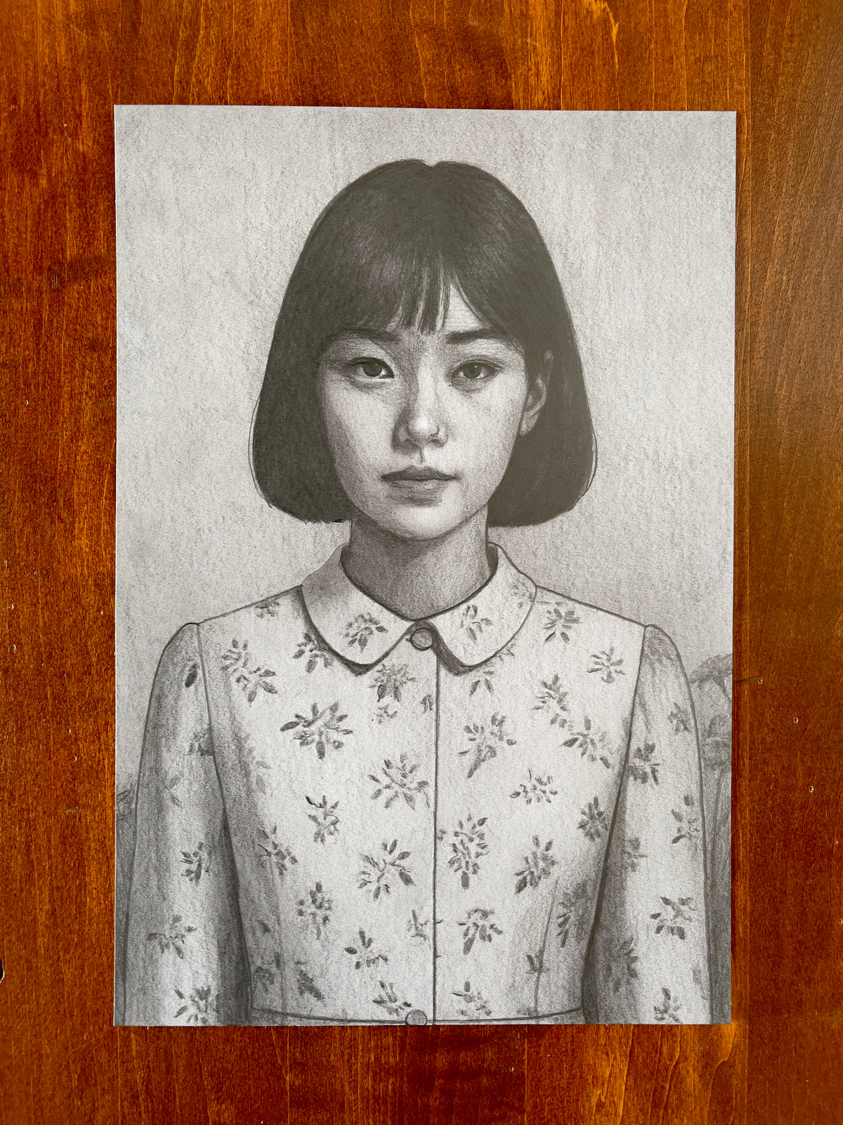 Seth Jennemann MEFREEK Running In Circles In An Open Field – graphite drawing in hyperreal pop surrealism style portraying a young woman with a straight bob haircut wearing a floral-patterned collared dress, blending innocence and quiet melancholy through delicate realism.
