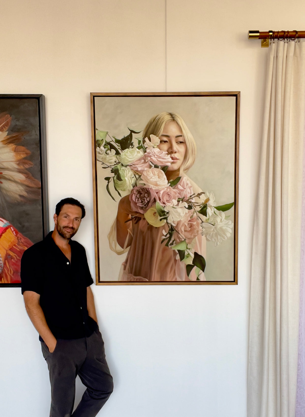 Seth Jennemann MEFREEK Elizabeth Lizzie Jennemann  Nguyen oil painting hyperreal contemporary portrait featuring a blonde woman in a sheer pink dress surrounded by lush white and blush roses, held close to her face, with Seth Jennemann standing beside the artwork in the gallery.