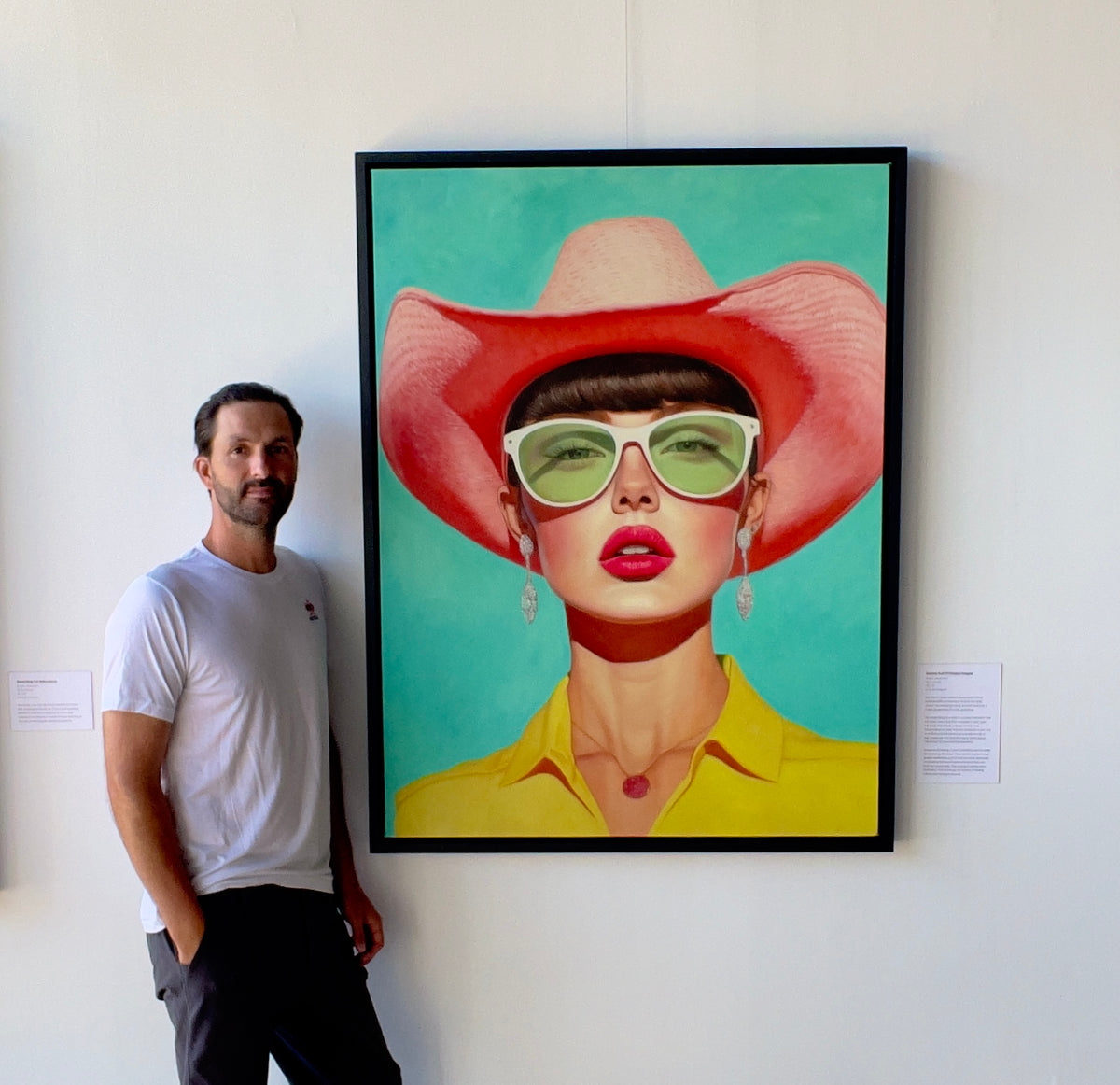 Seth Jennemann MEFREEK Rooms Full Of Empty People oil painting hyperreal pop surrealism contemporary portrait featuring a stylish woman in oversized green sunglasses, bright pink cowboy hat, bold pink lipstick, and yellow collared shirt on a vibrant turquoise background, with Seth Jennemann standing next to it in the gallery.