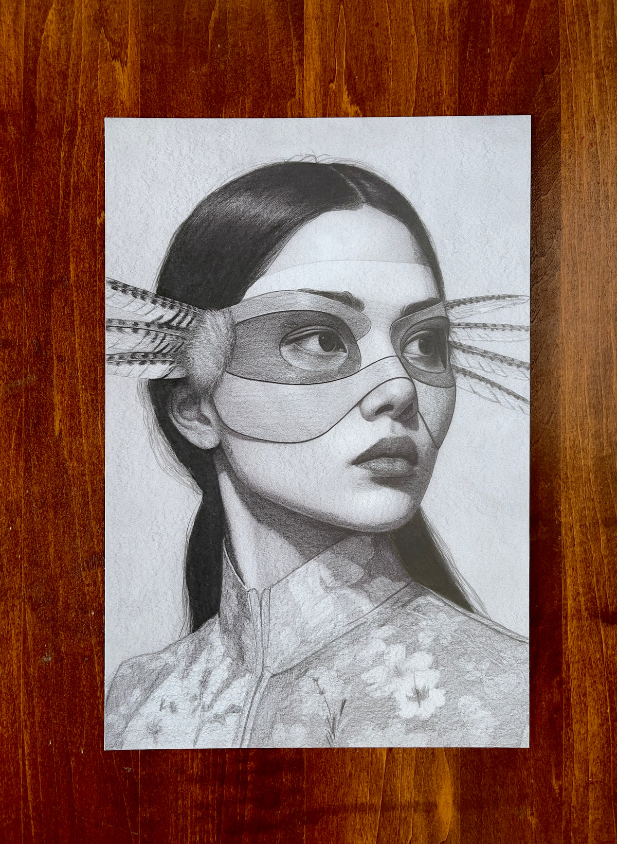 Seth Jennemann MEFREEK - She Likes It Better Wrong - graphite drawing in hyperreal contemporary portrait style depicting a woman in a floral-patterned high-collar garment wearing a sleek mask with feathered extensions, rendered with lifelike precision and tonal depth.
