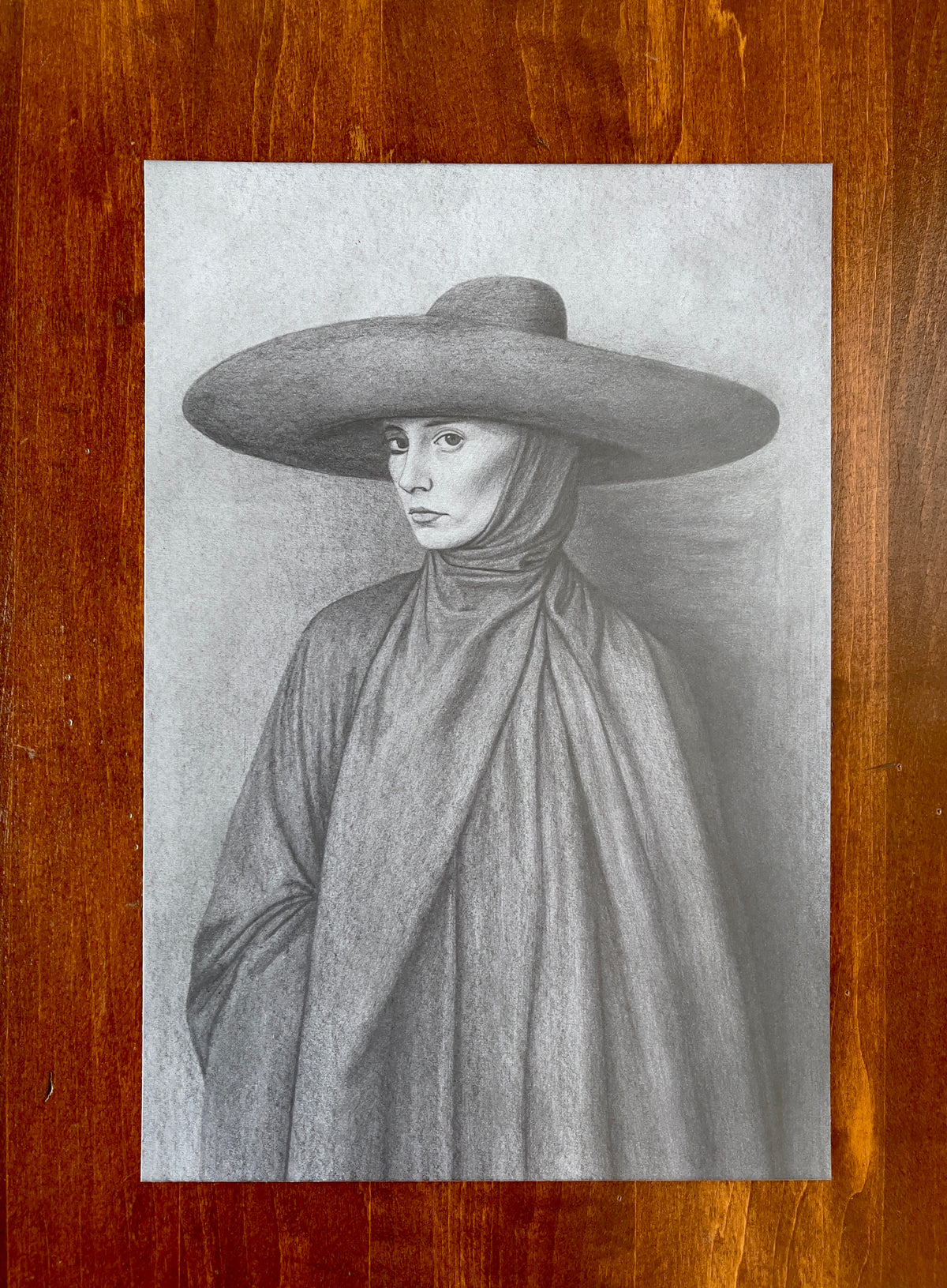 Seth Jennemann MEFREEK The Linger Of Apology – graphite drawing in a hyperreal contemporary portrait style depicting a solemn woman wearing a large circular hat and elegantly draped fabric, her gaze turned sideways beneath soft lighting that accentuates the folds and textures of the cloth.
