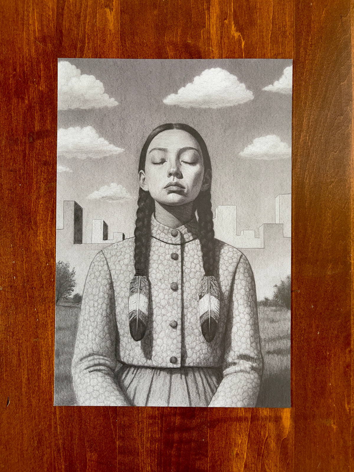 Seth Jennemann MEFREEK — Unholy Choirs and Unwanted Updates, graphite pencil drawing in hyperreal contemporary portrait style. A serene young woman with braided hair and feather ties sits with eyes closed against a surreal cityscape and soft cloud-filled sky.