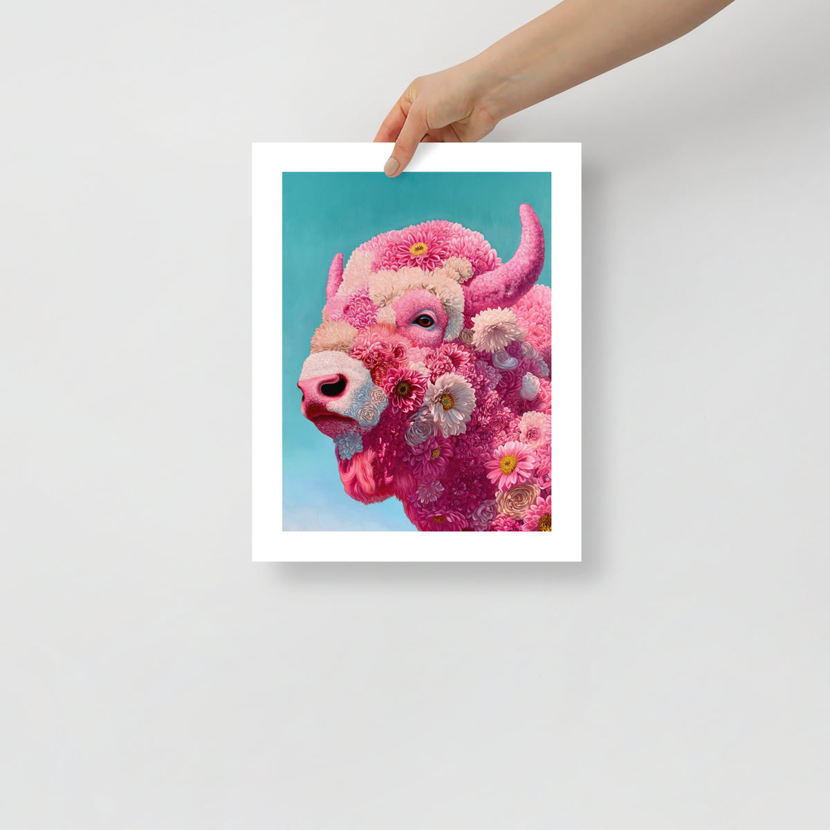 MEFREEK Seth Jennemann Open Edition Print hyper realistic floral bison portrait with intricate pink flowers forming the animal’s face, detailed horn and soft teal background, shown as a physical fine art print held by a hand against a minimal neutral backdrop