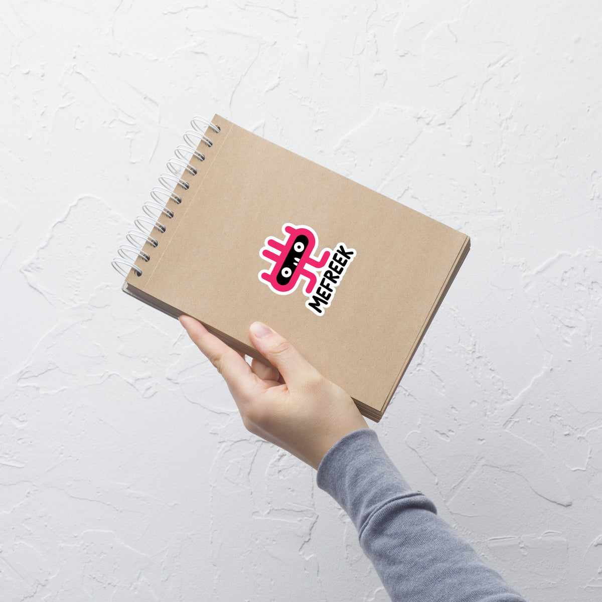 Hand holding a brown notebook with a logo on a light gray textured background