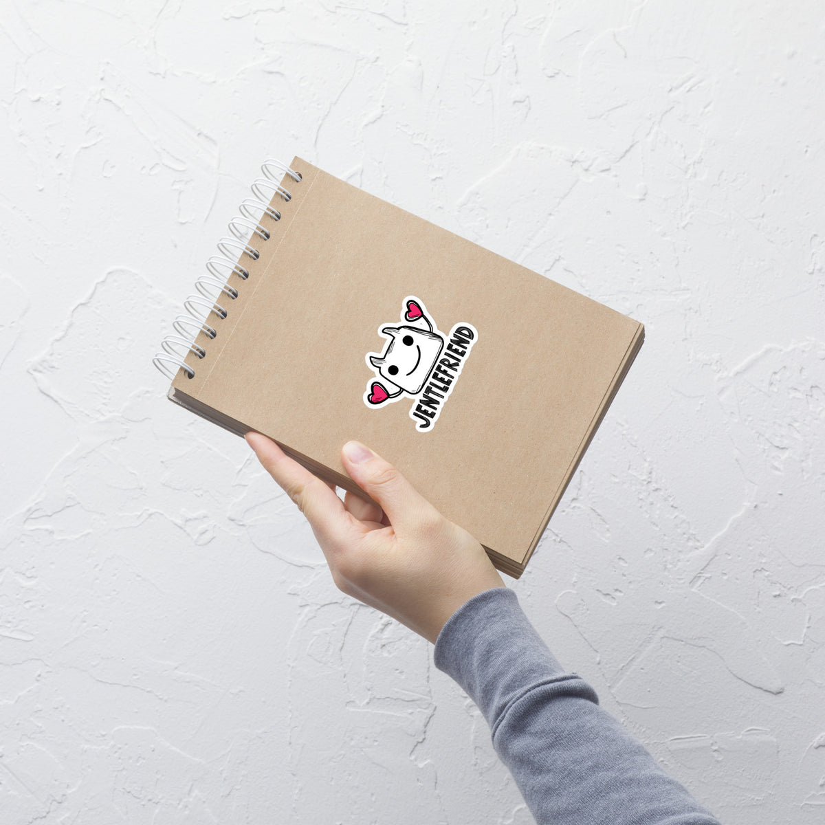 Hand holding a brown notebook with a logo on a light gray background