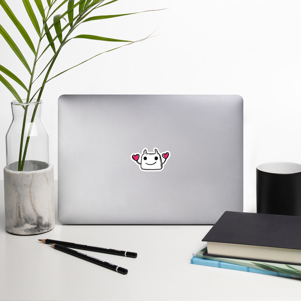 Laptop with a brand logo on a white surface with a plant, notebook, and pencils.