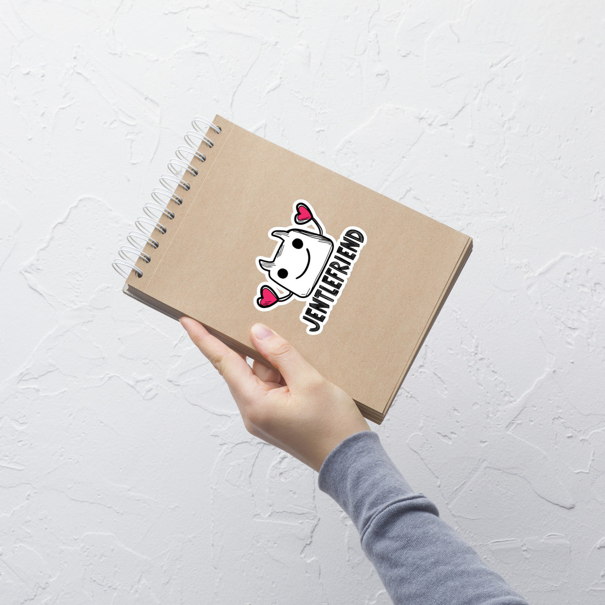 Notebook with a cartoon character and 'Jenifer' text held by a hand on a light gray background
