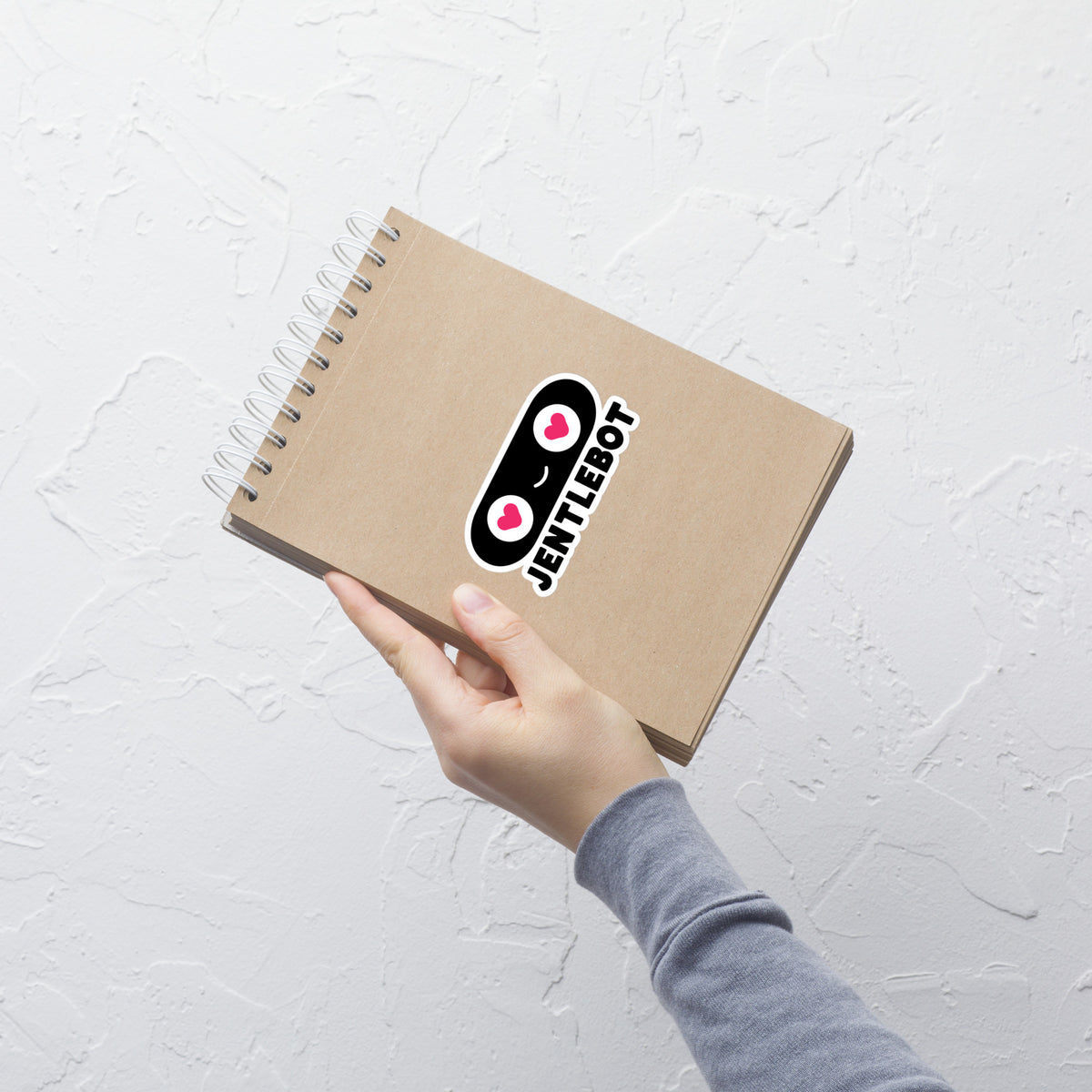 Hand holding a brown notebook with a logo on a light gray background