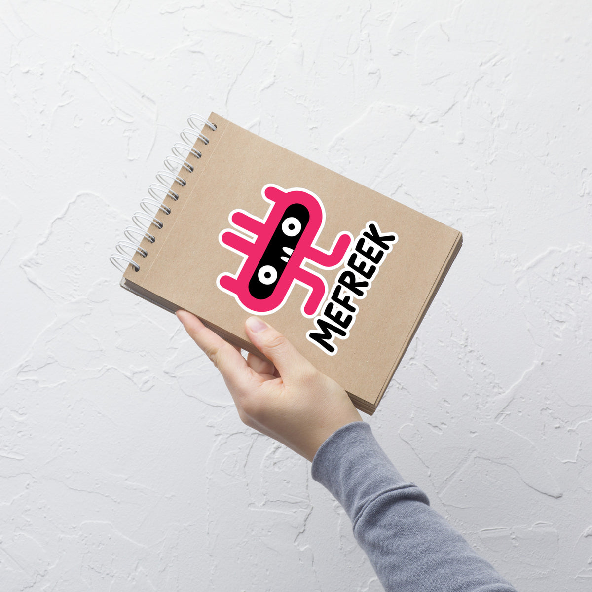 Notebook with 'Mefreek' logo held by a hand on a light gray background