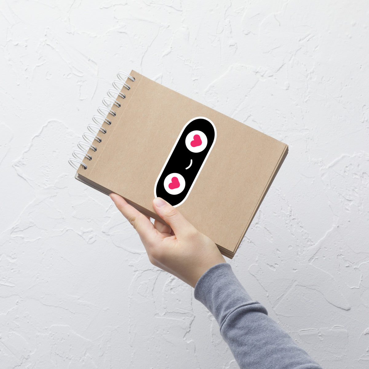 Hand holding a brown notebook with a decorative sticker on a light gray background