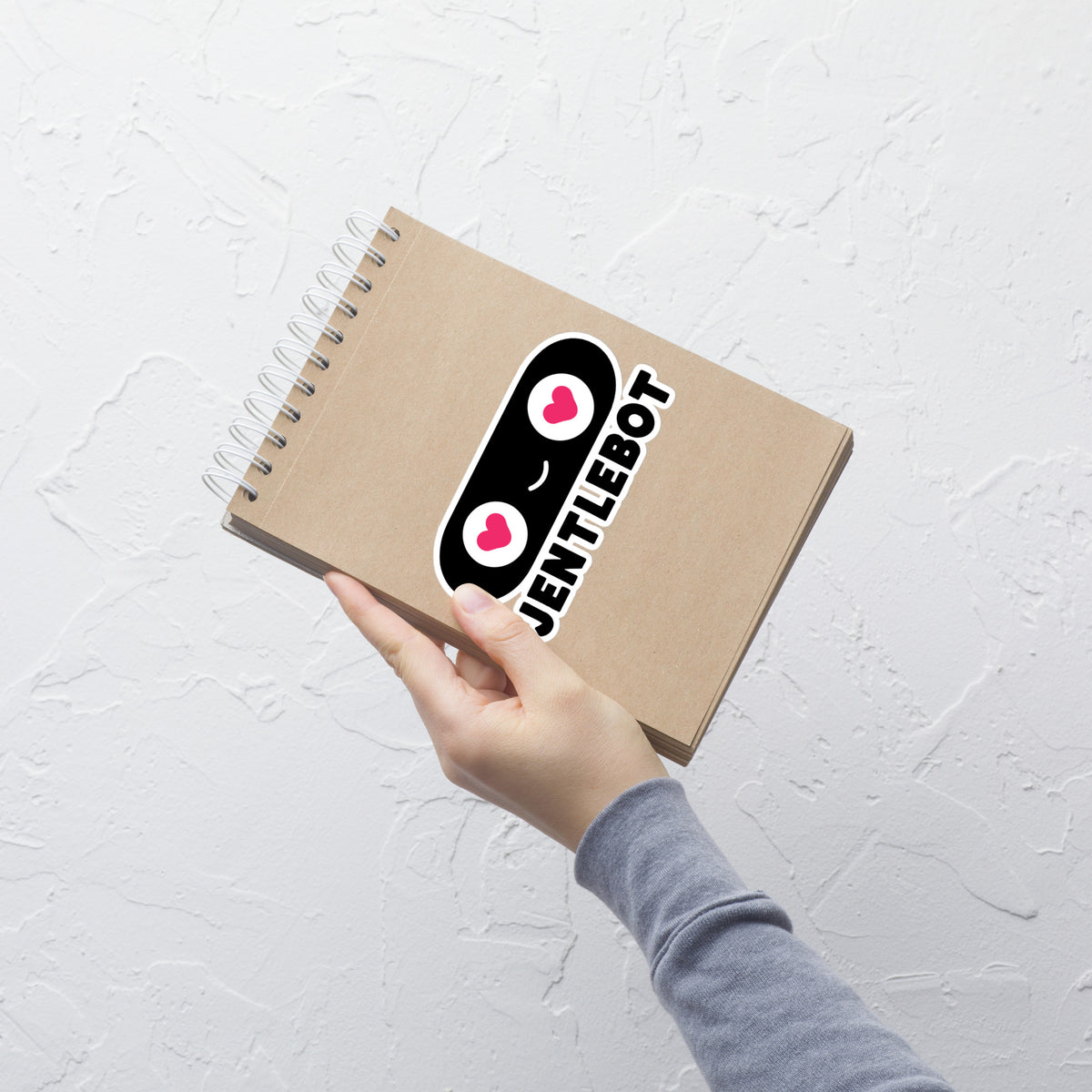 Notebook with a 'Jentlebot' sticker held by a hand on a light gray background