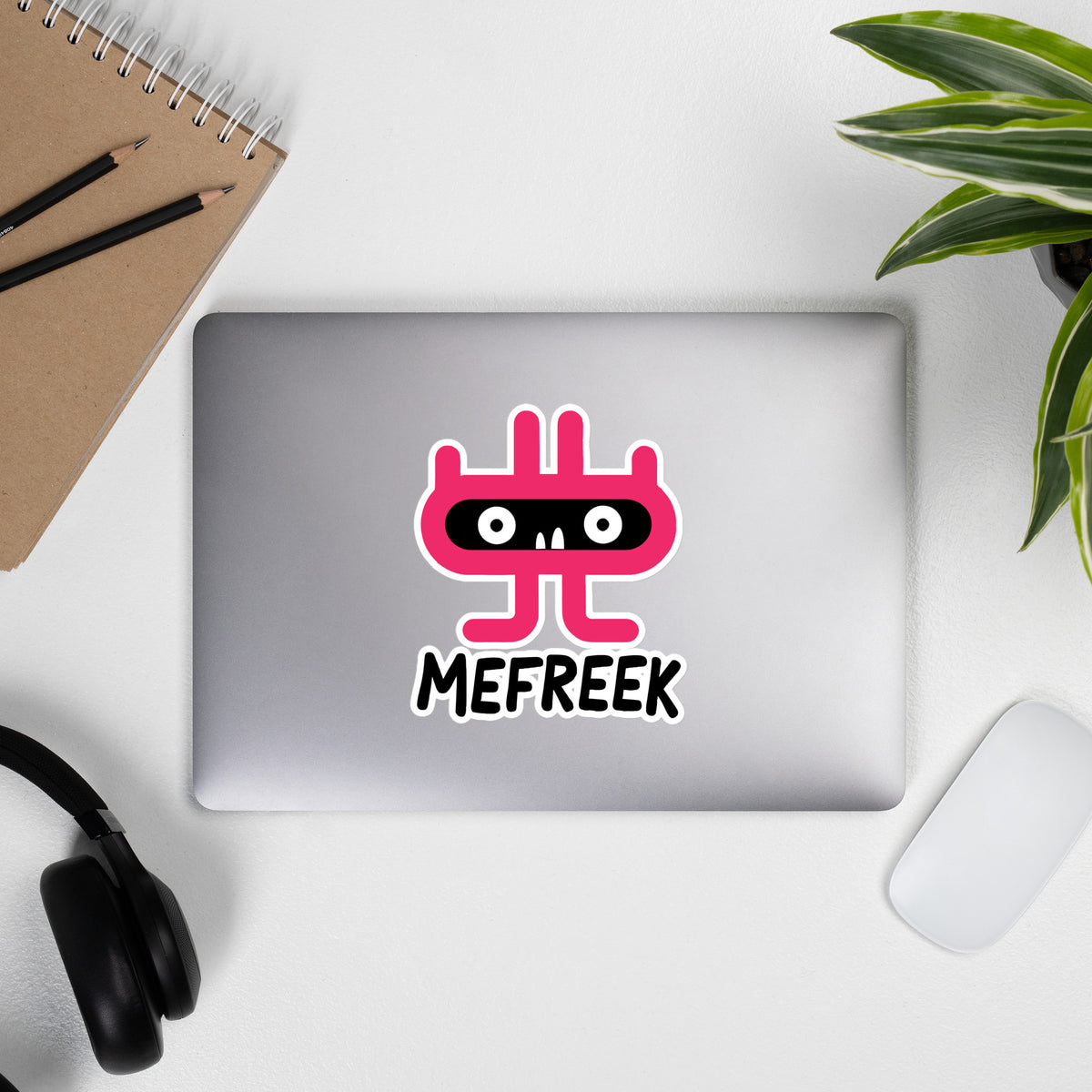 Laptop with a pink and black logo on a white surface with a notebook, pencils, and plant.